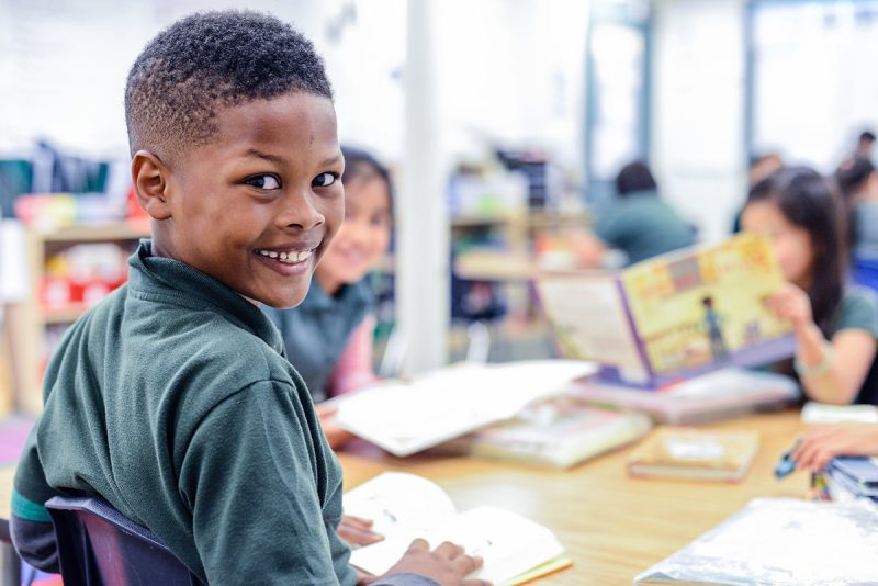 Open Up Resources EL Language Young Black student smiling and happy to be with classmates reading to each other