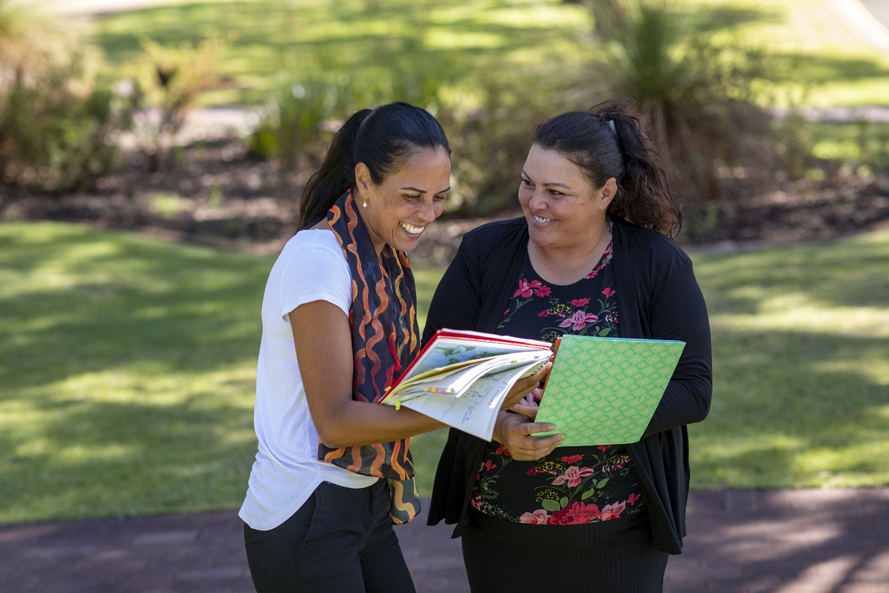 Two women sharing a joyful moment while looking at a book outdoors.